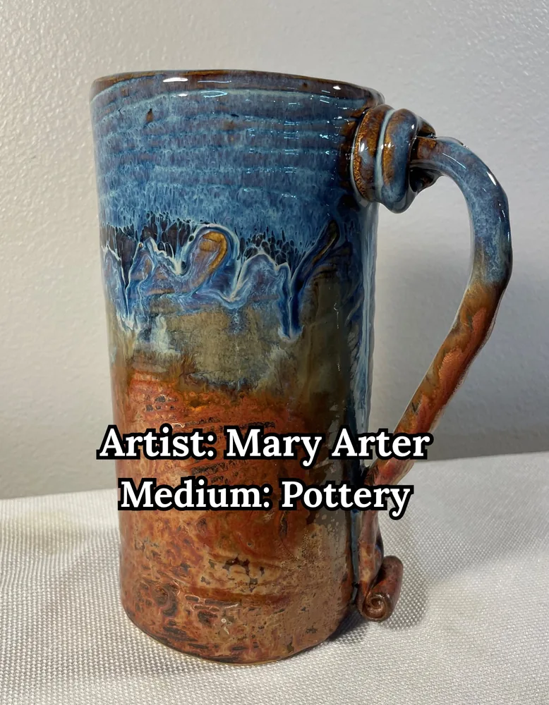 Tall glazed mug with blue drips flowing over rust red and a knotted handle, by Mary Arter