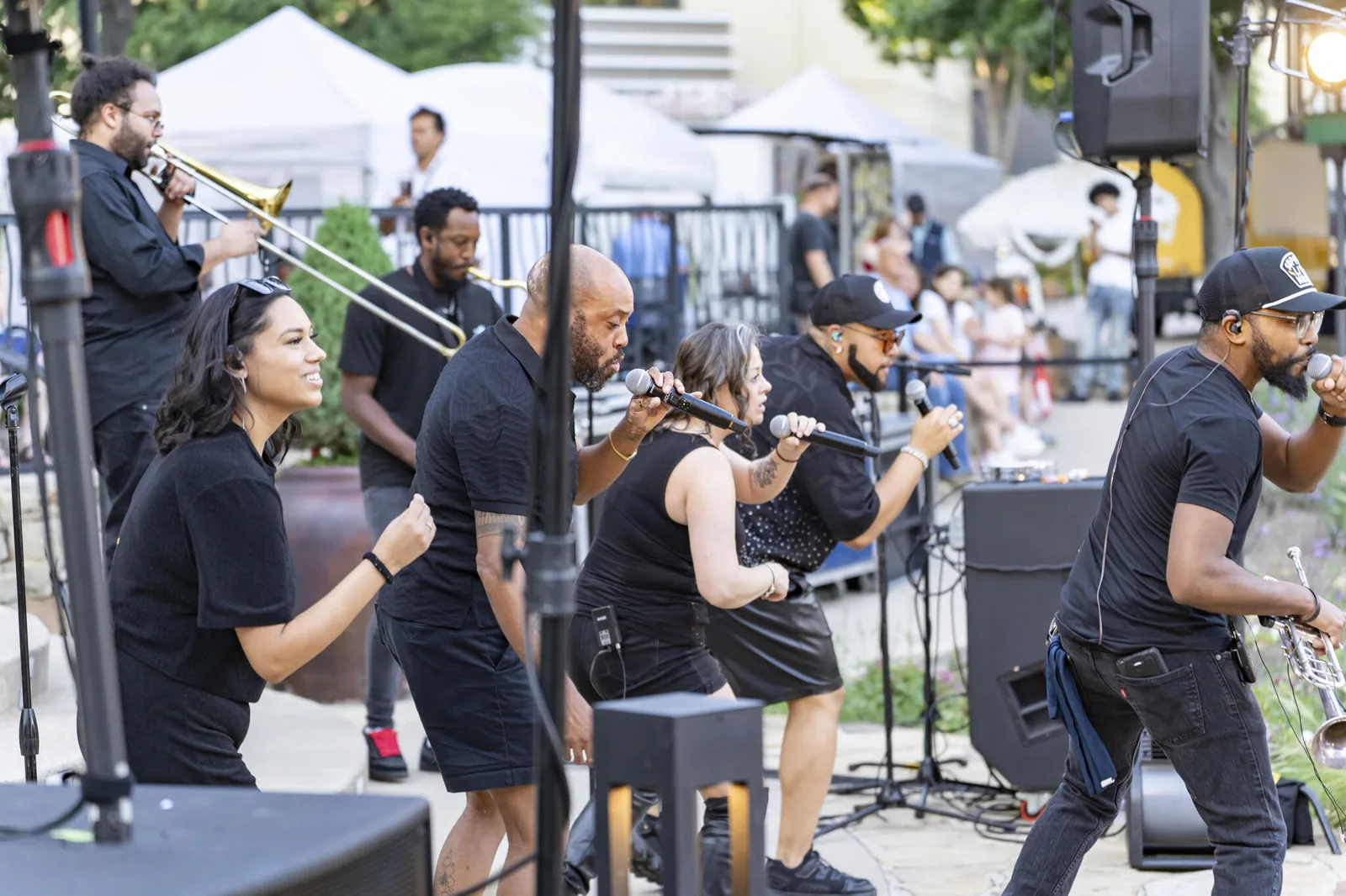 A vocal group with a horn section performs together beside the stage