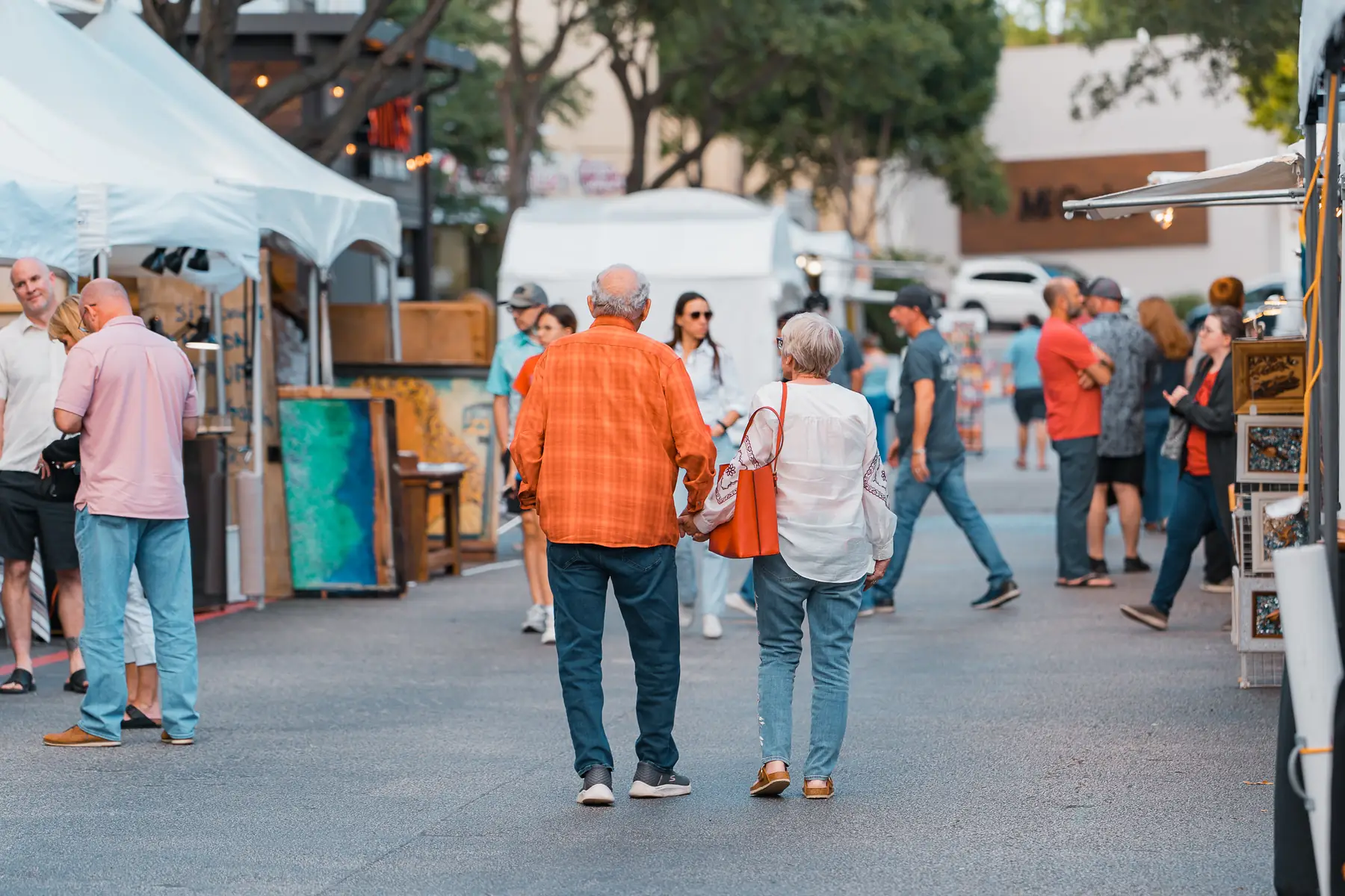 An older couple holds hands walking between artist booths at the festival