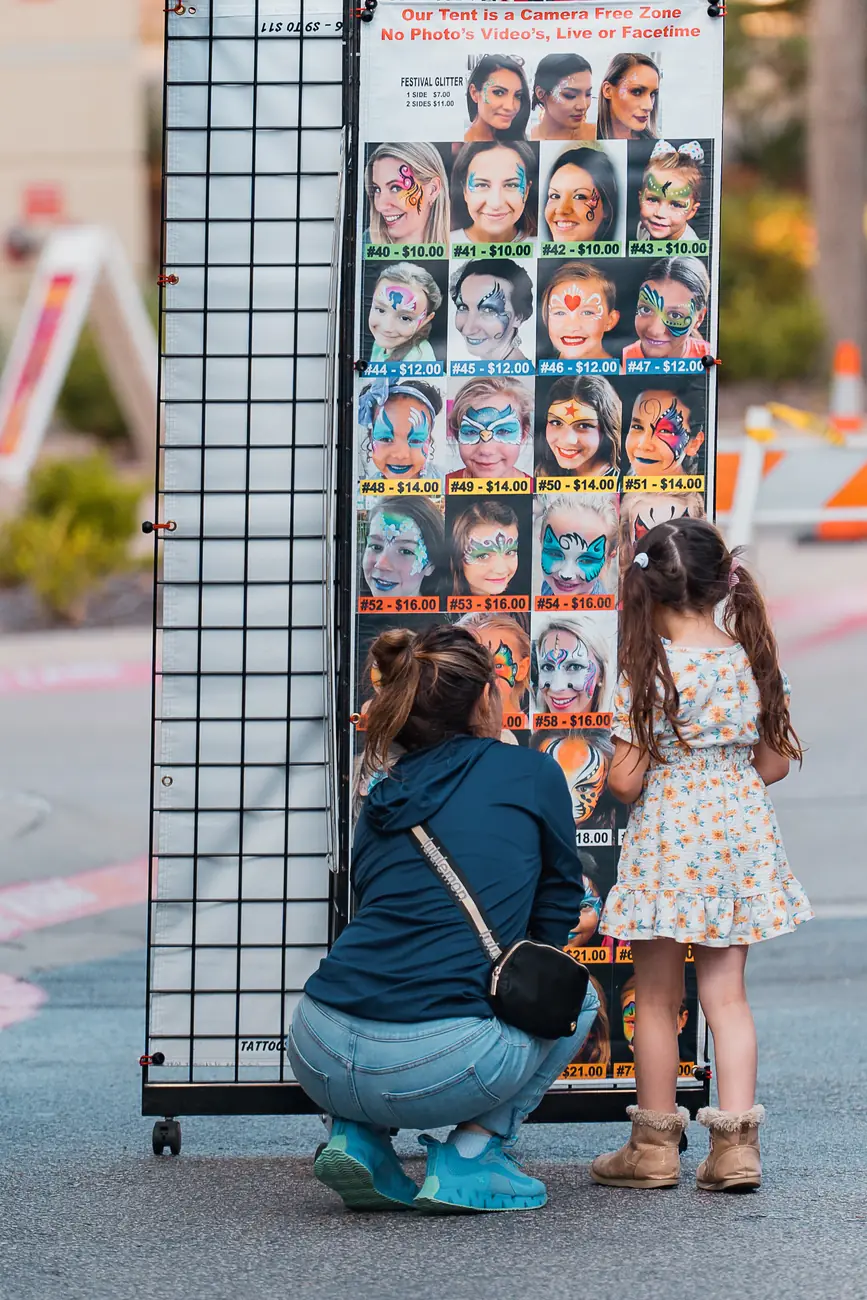 A parent and child choosing a design at the face-painting stand