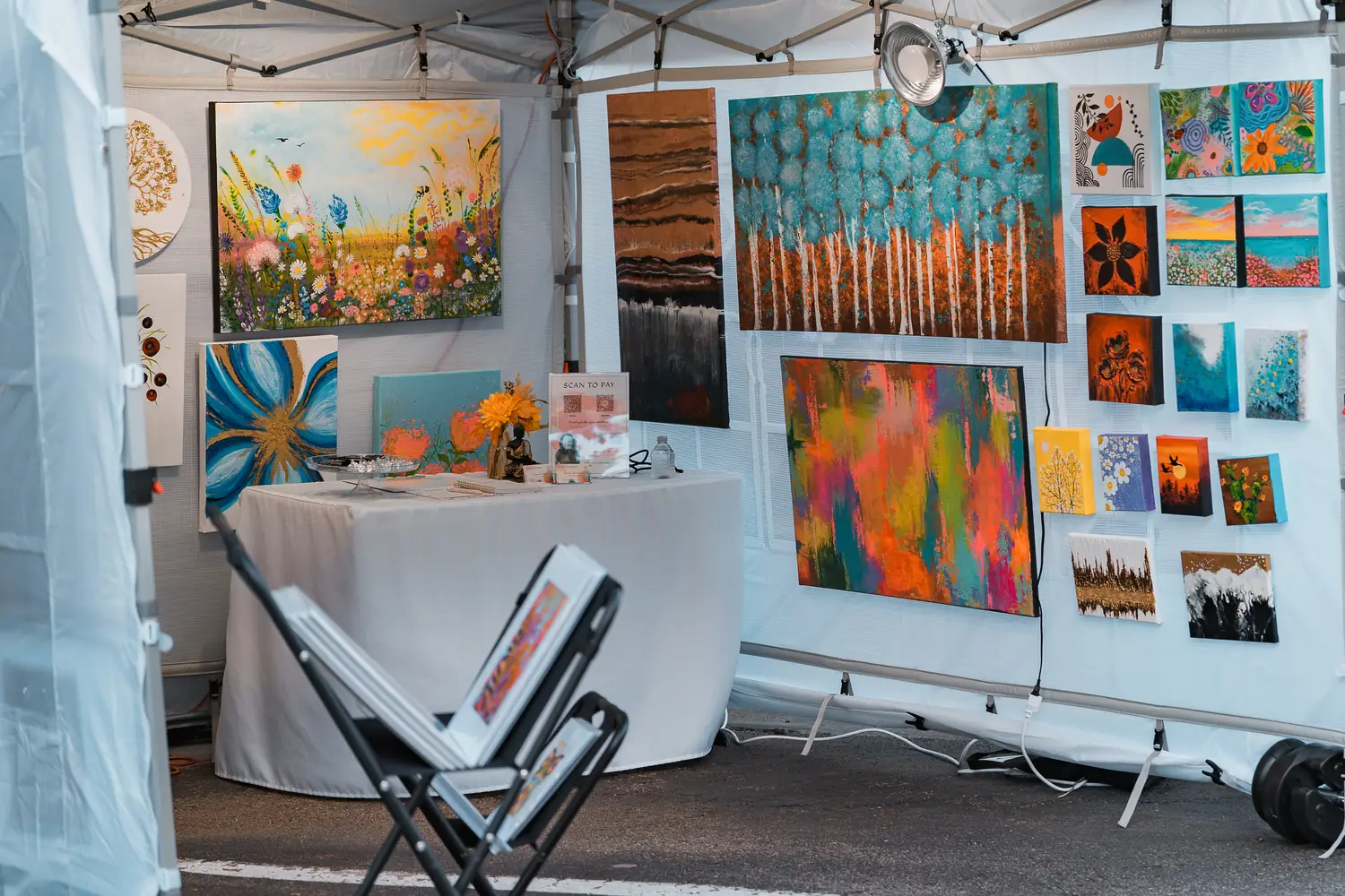 An artist's festival booth hung with colorful abstract and floral paintings
